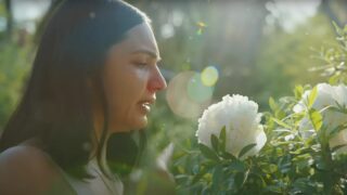 In a Geico ad, a woman – Jenna Jimenez – with a stuffy nose is smelling flowers in a garden.