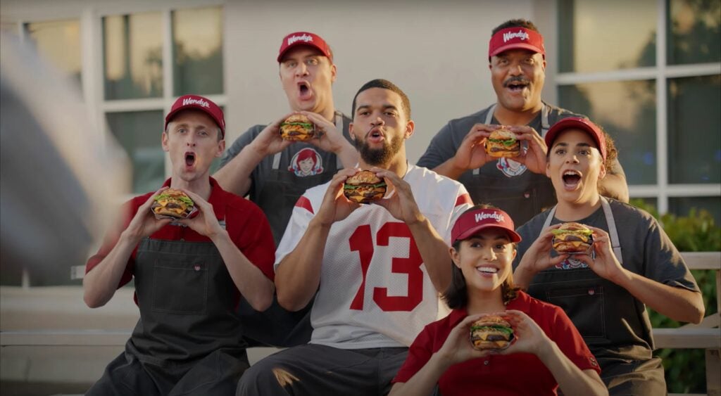 A group of people posing for a Wendy's ad with burgers.