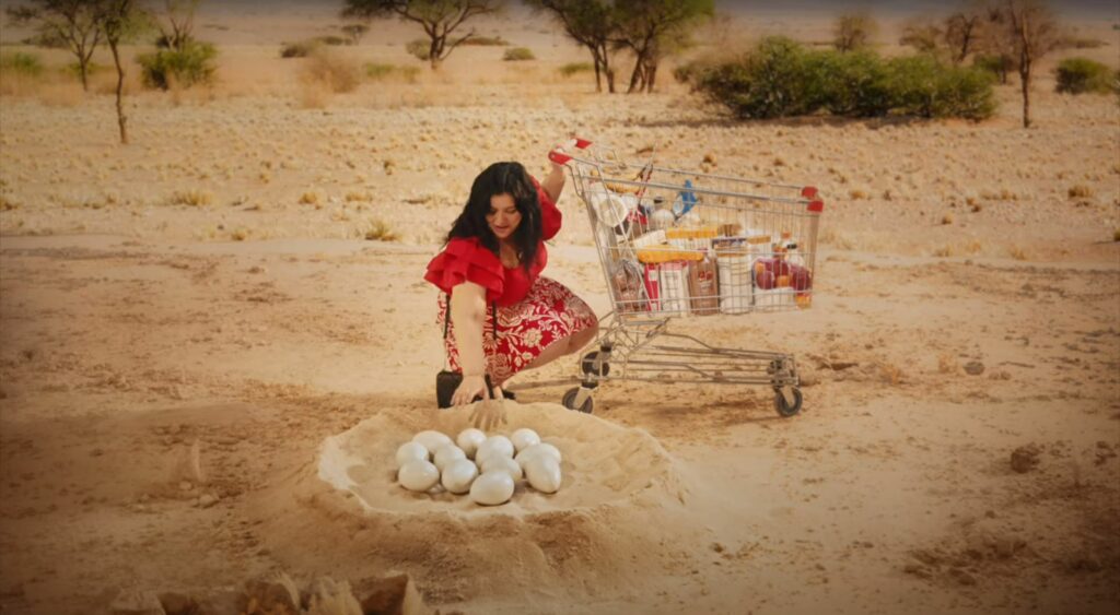 A woman with a shopping cart experiences a humorous encounter in the desert.
