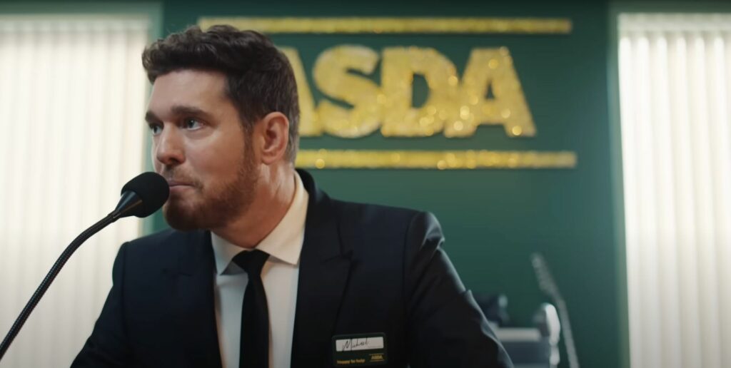 A man in a suit speaking into a microphone during the Asda Christmas Commercial 2023.
