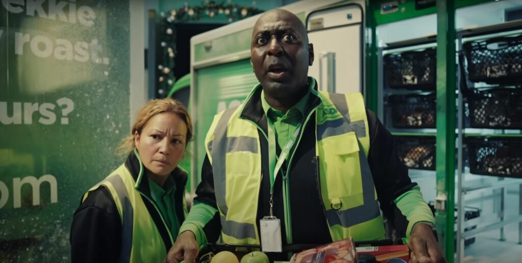 Two people in green vests standing in front of a refrigerator for the Asda Christmas Commercial 2023.