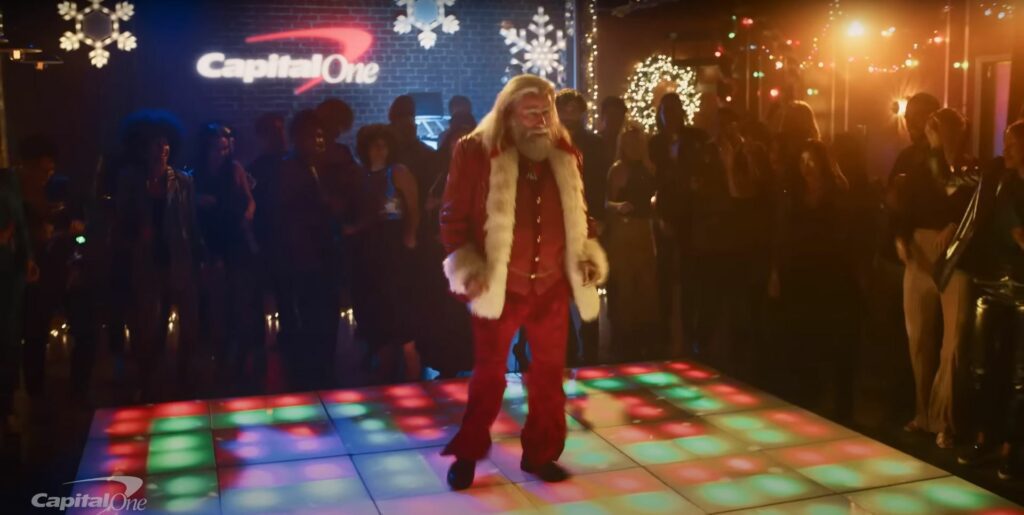John Travolta, dressed in a red suit reminiscent of Christmas, is dancing gracefully on a disco floor.