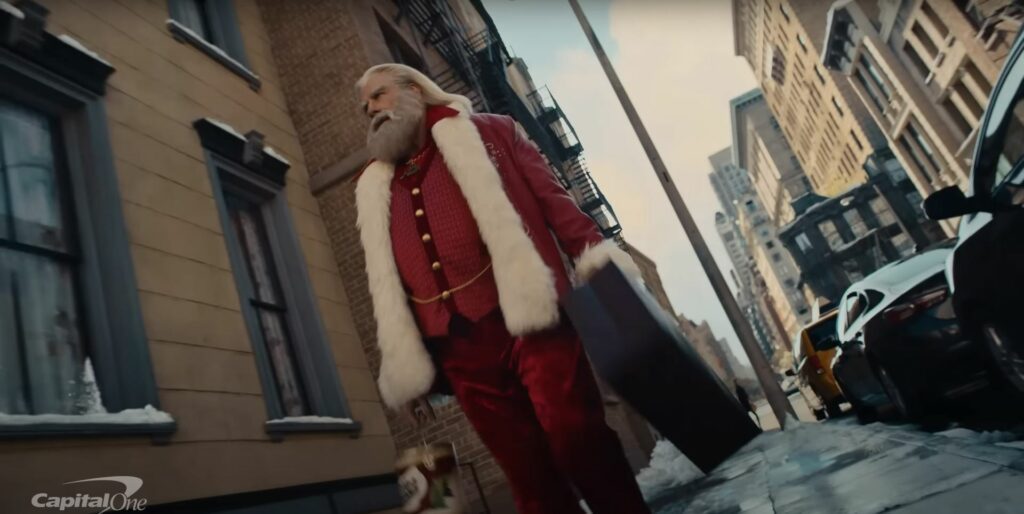 In the year Christmas 2023, John Travolta portrays Santa Claus in a suit as he gracefully walks down a bustling city street.