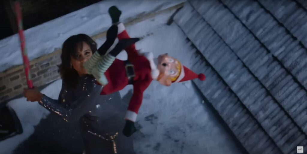 A woman is holding a Santa Claus doll in the snow for a Christmas ad.