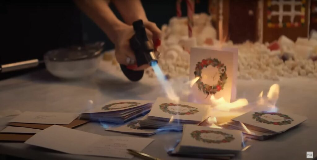 A person is lighting a candle on a table of cards in a Christmas ad for Marks & Spencer's 2023 campaign.