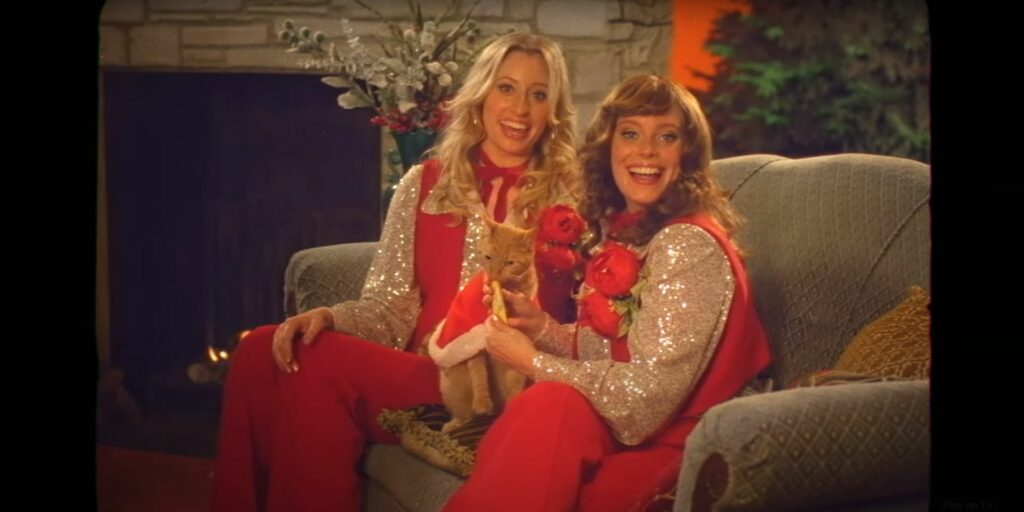 Two women in red sitting on a couch for a Christmas ad.