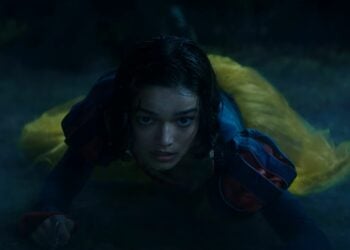 In the dark, misty environment of the Snow White 2025 movie trailer, a person wearing a yellow and blue outfit is seen lying on the ground, looking ahead amidst controversy.