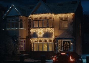 The house is adorned with white string lights, casting a festive glow for Christmas. A car sits in the driveway, completing the serene scene, reminiscent of a classic Sky Cinema holiday advert.