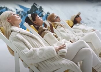 Four people in chic winter clothing, part of the 2024 Gucci Holiday Campaign, are reclining on chairs amidst a serene snowy landscape.