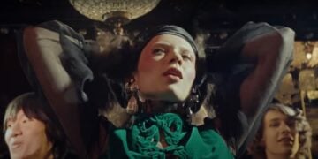 A person in a green outfit poses nostalgically with hands on their head under a chandelier, evoking the charm of a Valentino Holiday. In the background, two others capture the essence of the Holiday Ad 2024.