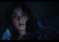 A woman lies in bed at night, illuminated by the glow of her smartphone as she scrolls, capturing a scene straight out of a faux horror trailer—Goodnight Phone.