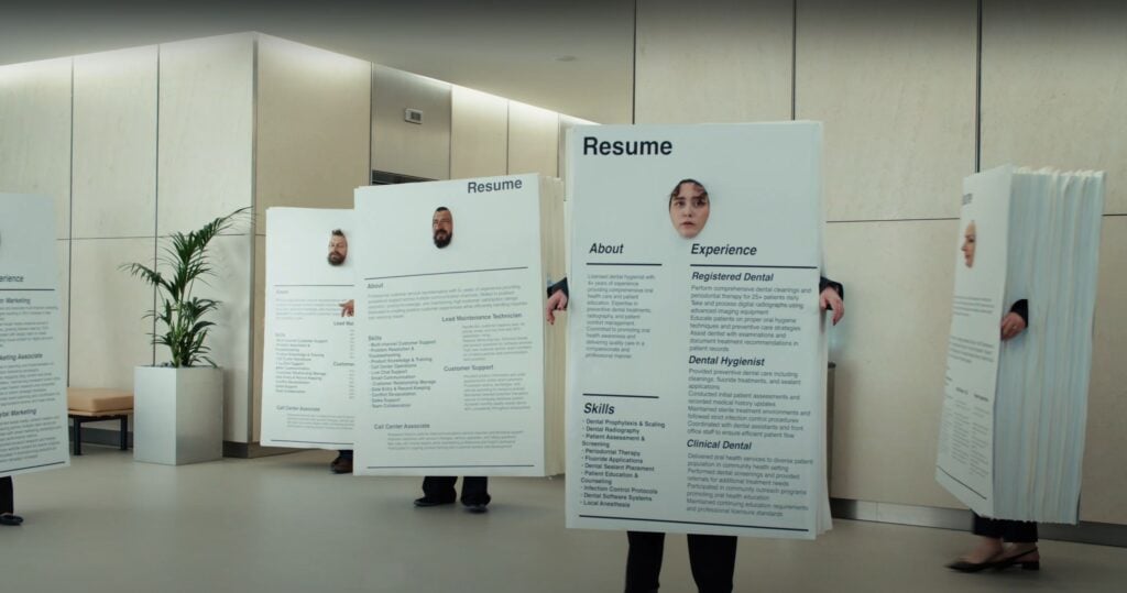 Business professionals in an office lobby hold oversized resume boards featuring profile photos and text, as if participating in a 2025 Indeed Career Scout event.