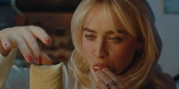 A woman with blonde hair and red painted nails is eating a stack of potato chips, holding them near her mouth—just like Sabrina Carpenter might during the Pringles Super Bowl 2026 commercial.